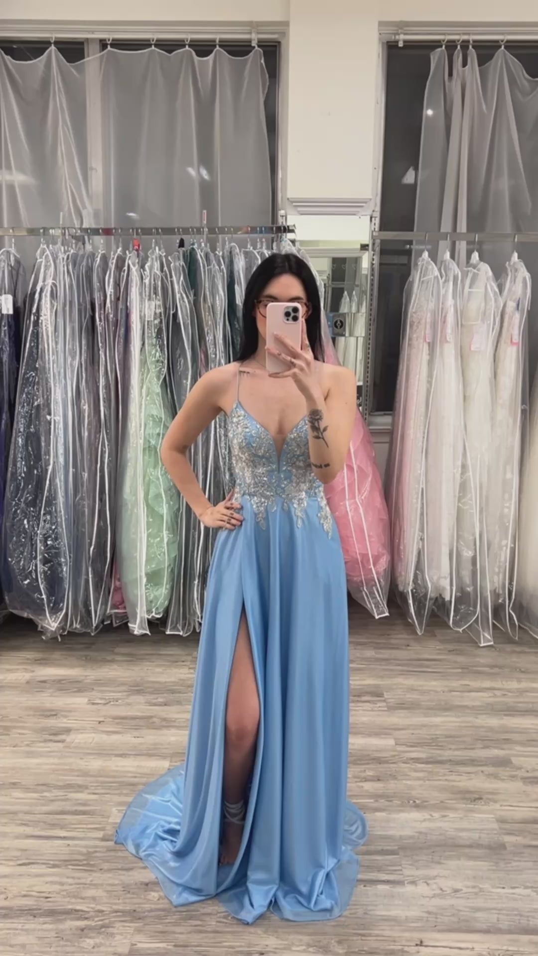 Woman wearing a blue evening gown with a high slit in a fitting room.