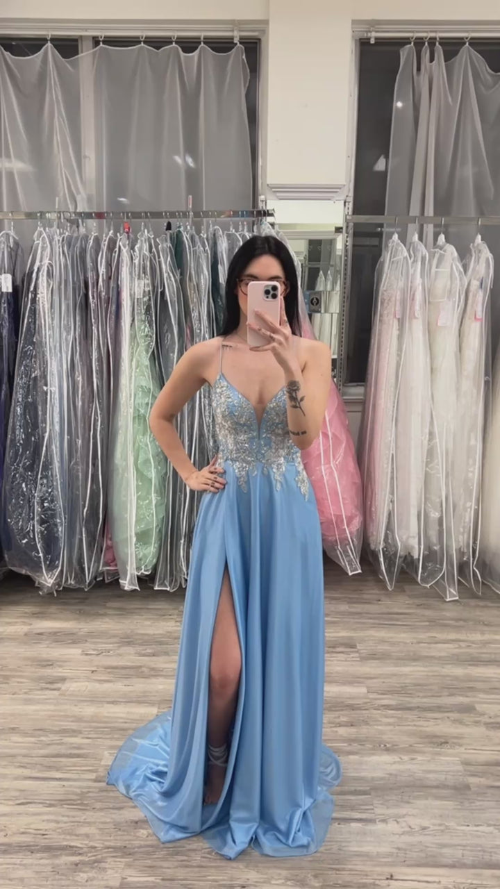 Woman wearing a blue evening gown with a high slit in a fitting room.
