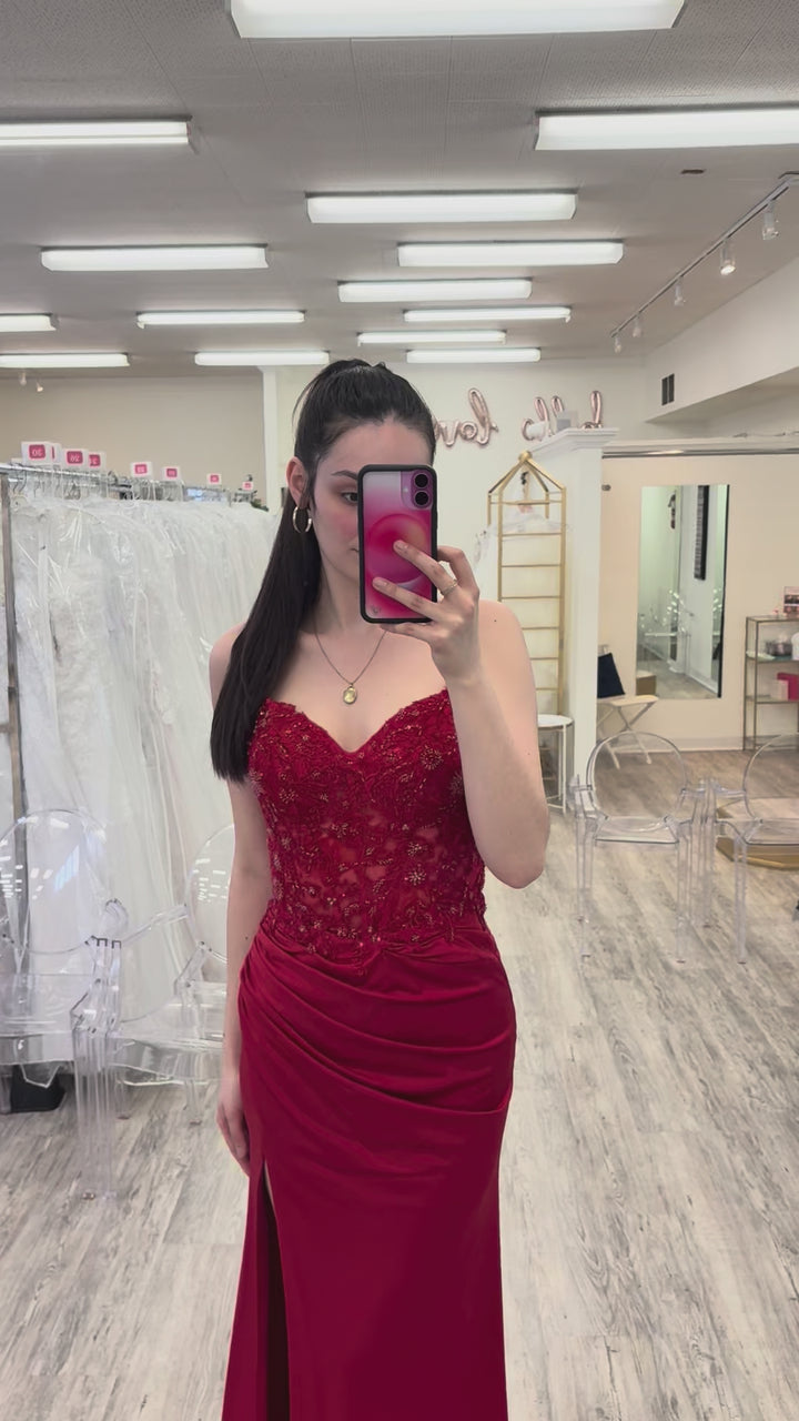 Woman in a red evening gown taking a mirror selfie in a fitting room.