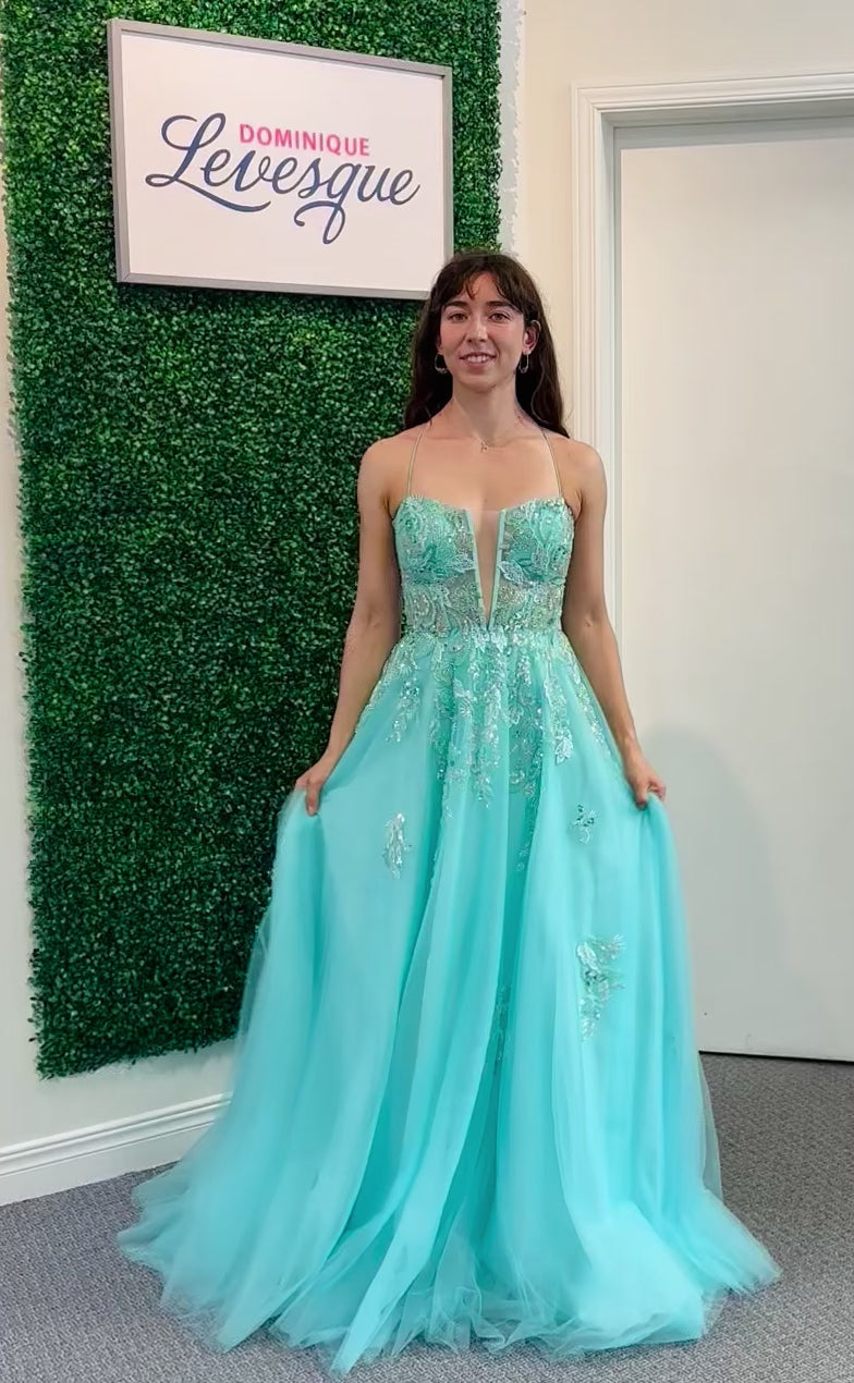 Woman in a aqua evening gown with floral details, standing against a green leafy wall.