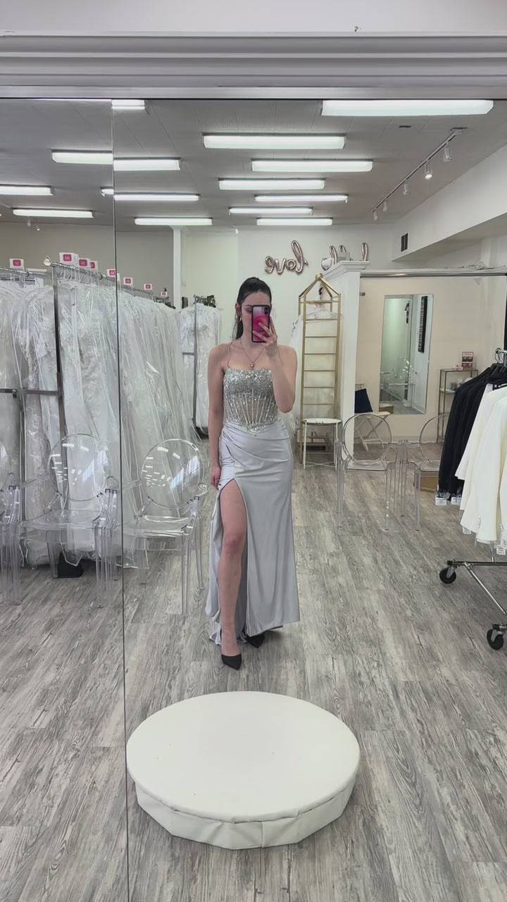 Woman wearing a silver evening gown in a store setting.