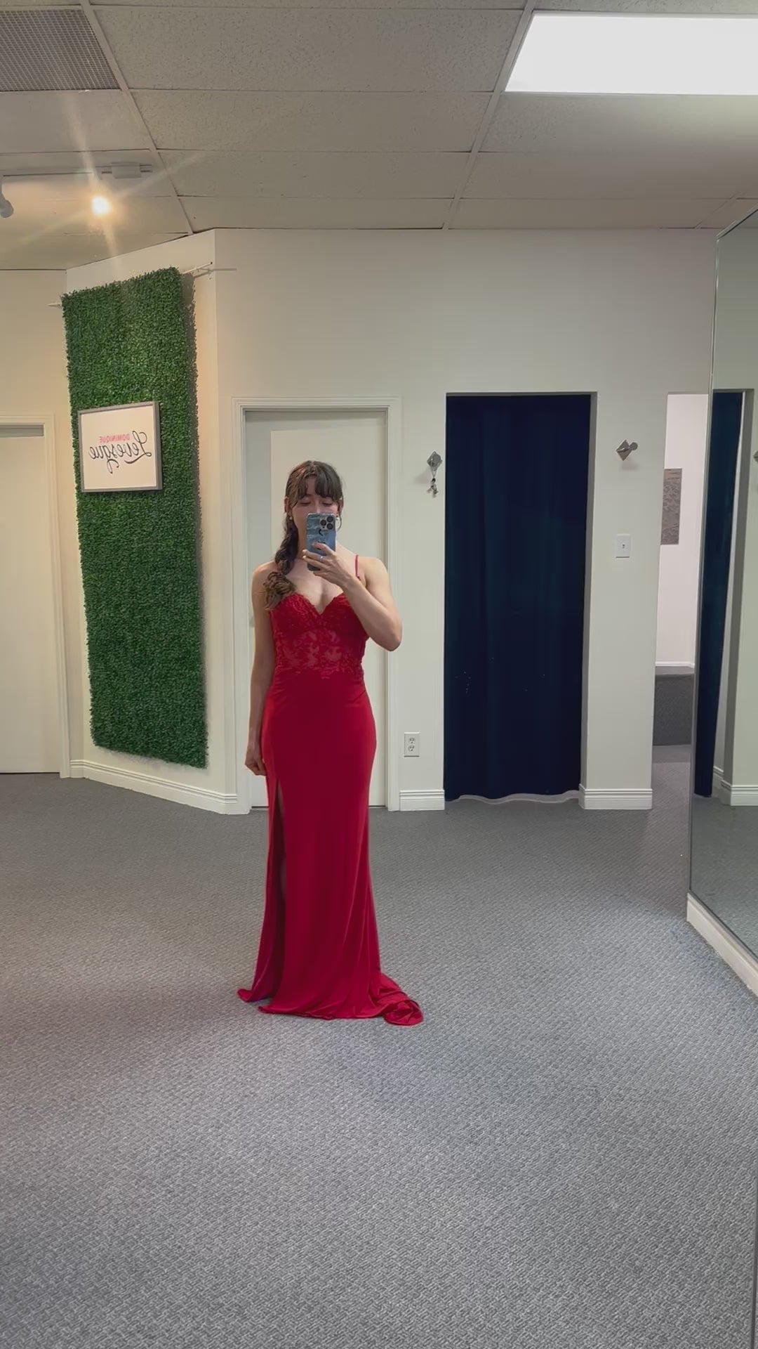 Woman in a red evening gown taking a mirror selfie in a fitting room.