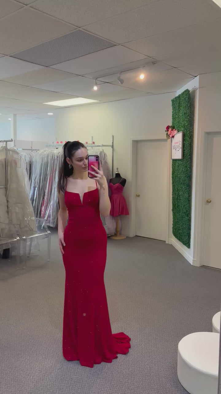 Women wearing a red dress in a fitting room with mirrors and clothing racks.
