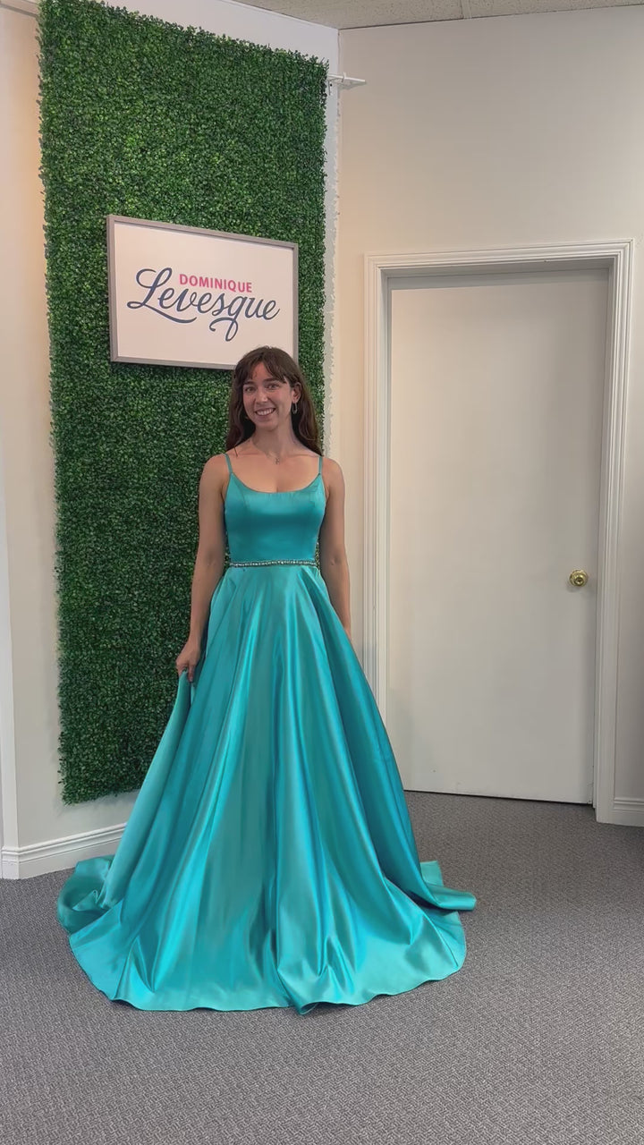 Woman in a blue evening gown standing against a green wall with a sign.
